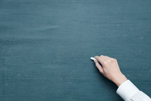 Hand holding chalk ready to write on a blank blackboard surface.